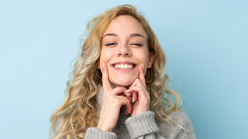 Young blonde woman pointing to her flawless smile