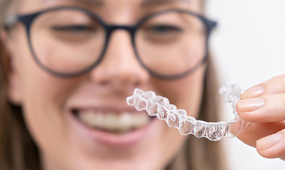 Young woman with glasses holding a clear aligner