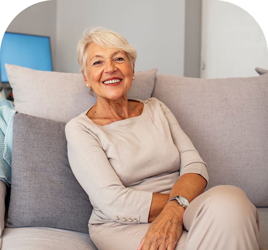 Senior woman smiling on her couch after replacing missing teeth in Burbank