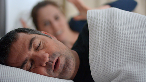 Frustrated woman in bed next to a snoring man